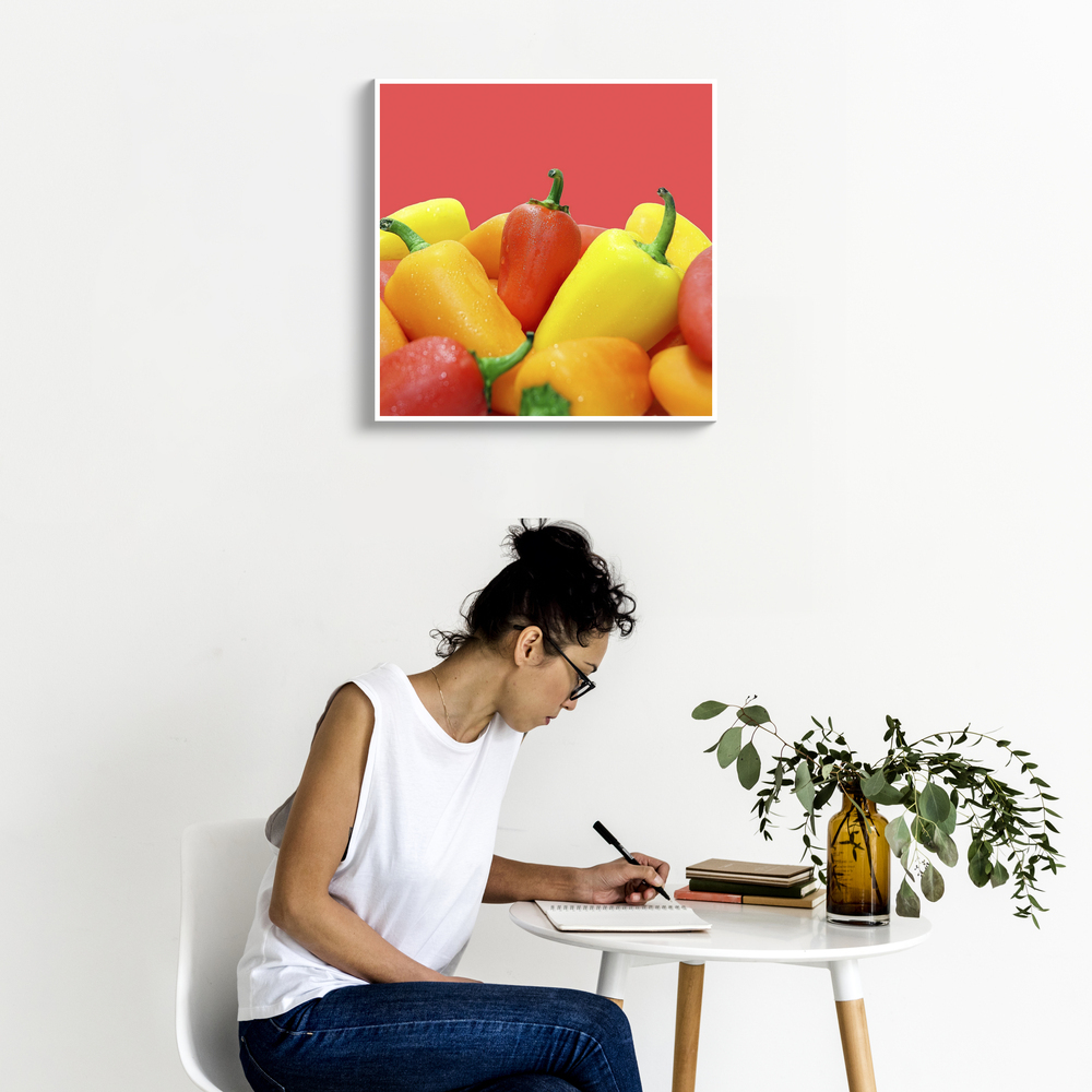 Fotoleinwand mit bunten Paprikas auf rotem Hintergrund an einer weißen Wand über einem kleinen Tisch