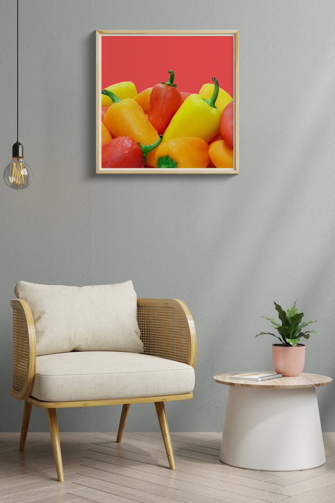 Fotoleinwand mit bunten Paprikas im hellen Holzrahmen an einer grauen Wand über einem Sessel