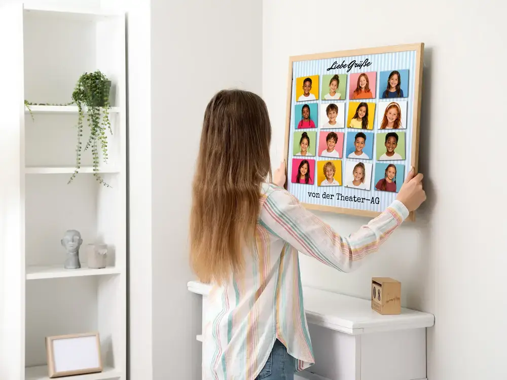 Fotocollage der Theater-AG mit 16 bunten Kinderporträts und Grußtext im hellen Holzrahmen an einer weißen Wand