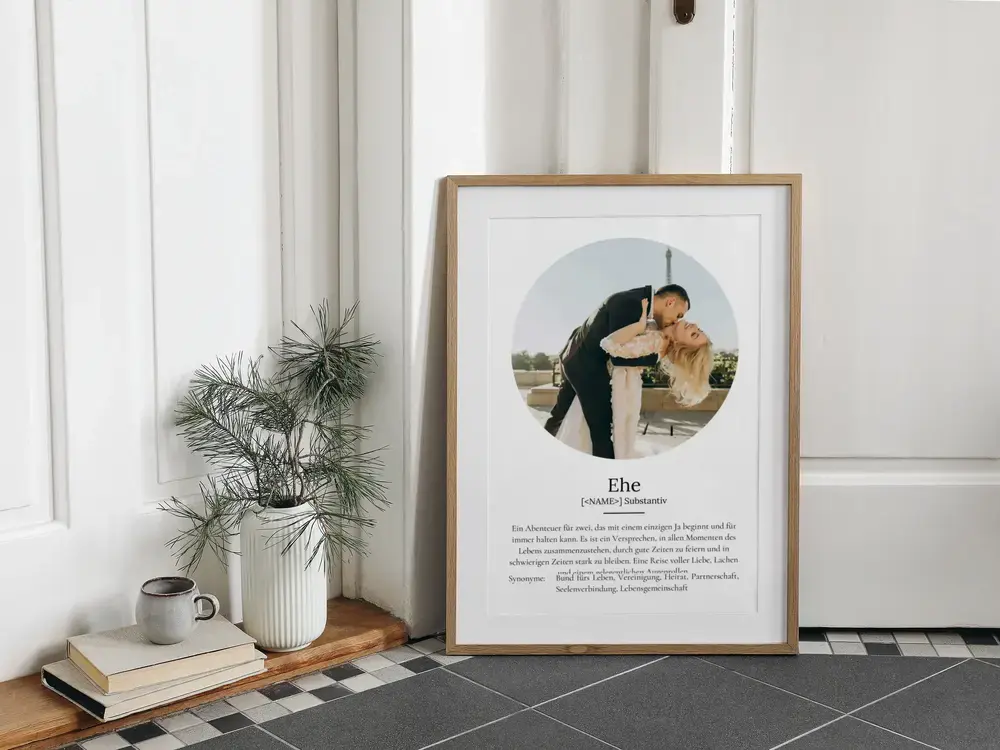 Definitionsposter zur Ehe mit rundem Brautpaarfoto im Naturholzrahmen, auf dem Boden neben Büchern und Vase