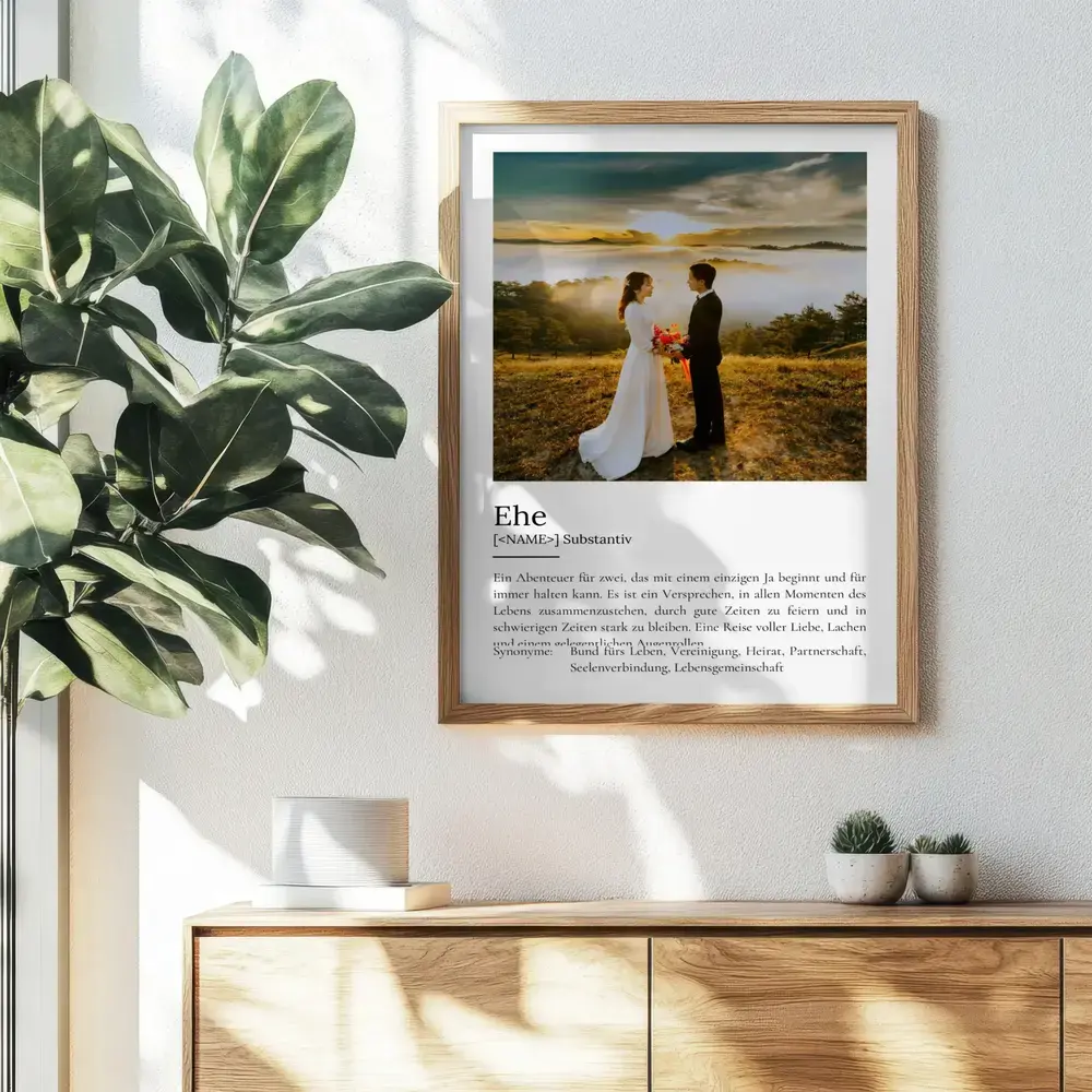 Definitionsposter zur Ehe mit großem Hochzeitsfoto im Holzrahmen an der Wand über einer Kommode neben einer Pflanze