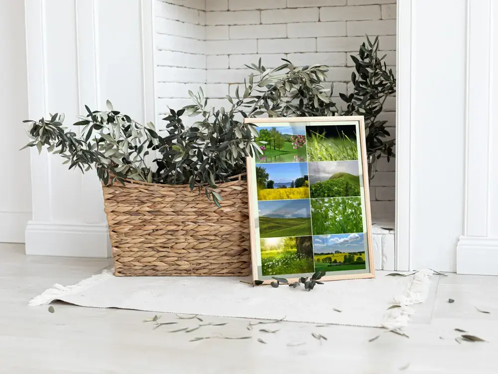 Gerahmte Natur-Fotocollage mit Wiesen und Rapsfeldern, auf dem Boden neben einem Pflanzkorb vor weißem Kamin